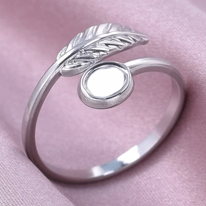Macro shot of silver feather ring with round bezel setting on light purple satin fabric