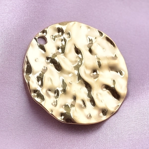 Minimalist gold hammer-textured 304 stainless steel round pendant on purple silk fabric