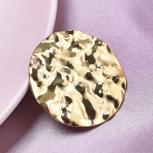 Macro shot of gold hammered round pendant with textured metallic finish on purple silk