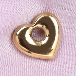 Gros plan du pendentif cœur doré sur velours rose montrant un poli miroir brillant