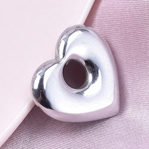 Vue macro d'un pendentif cœur en acier poli effet miroir sur fond satiné