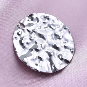 Detailed close-up of a silver hammered texture round pendant on purple silk fabric background