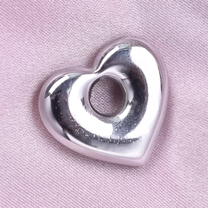 Détail du pendentif cœur évidé en acier inoxydable 304 poli posé sur un tissu en soie rose