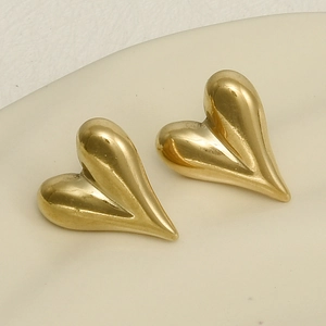 Detailansicht der goldenen 3D-Herzohrringe auf einem weißen Keramiktablett