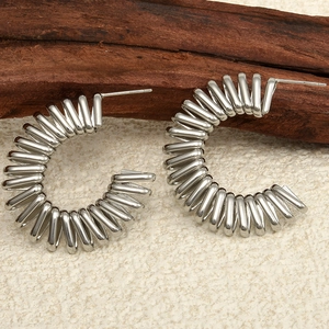 Détail des boucles d'oreilles créoles spirales en acier argenté sur bois foncé
