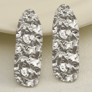 Close-up of silver long oval earrings with hammered metal texture on ceramic surface