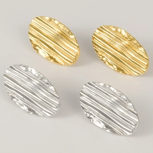 Dettaglio degli orecchini ovali plissettati in oro e argento su uno sfondo grigio chiaro