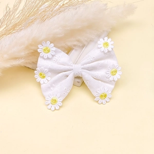 Détail d'une barrette à cheveux nœud blanc en tissu avec marguerites brodées et texture