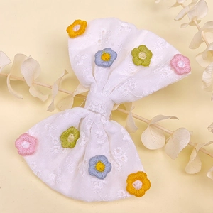 Détail d'une pince à cheveux nœud blanc avec des marguerites brodées colorées
