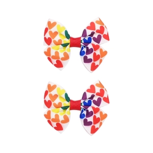 Dettaglio di due fermagli per capelli a fiocco con motivi a cuore arcobaleno per bambini