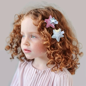 Detail view of cute glitter star hair clips worn by a young child on a grey background