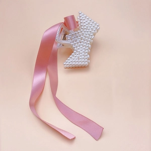 Close-up of elegant hair claw clip with white pearls and long pink satin ribbon streamer