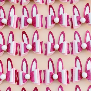 Pink glitter bunny ear hair clips with white pom-pom arranged in a pattern for Easter