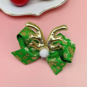 Detail of Christmas bow hair clip with golden antlers, snowflakes, and white pom pom
