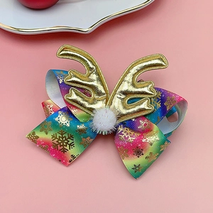 Close-up of Christmas bow hair clip with gold antlers and rainbow ribbon on pink background