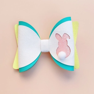 Detailed close-up of Easter bunny bow hair clip with white glitter and plush pom-pom tail