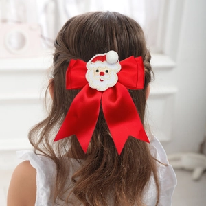 Detailed back view of a girl wearing a large red satin bow hair clip with Santa embroidery