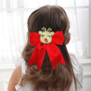 Detailed view of red silk bow hairclip with golden glitter reindeer on wavy brown hair