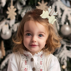 Detalle de pinza para pelo con purpurina, astas y lazo en una niña frente al árbol navidad