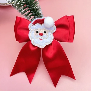 Close-up of red satin Christmas bow with Santa Claus embroidery on pink background