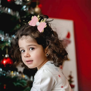 Close-up of child wearing pink Christmas bow hair clip with antlers and white pompom