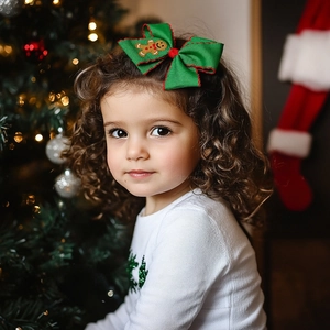 Close-up of a green gingerbread man hair bow with red stitching on a festive background