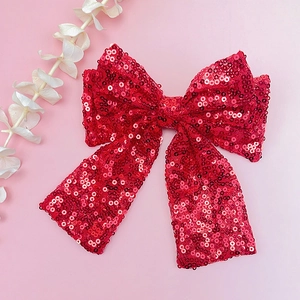 Dettaglio del fiocco per capelli con paillettes rosse lucide su sfondo rosa con fiori