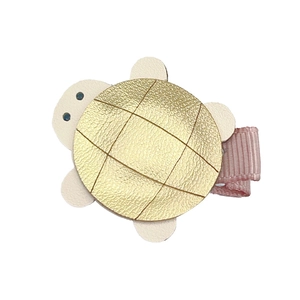 Detail of cute turtle hair clip with golden faux leather shell and pink ribbon wrap