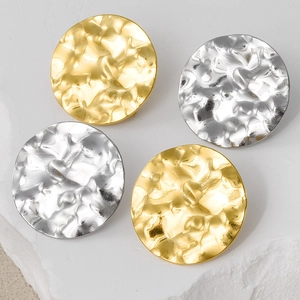 Detailed view of gold and silver round hammer textured earrings on stone pedestal