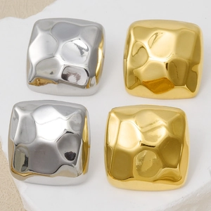 Detail of square hammered metal stud earrings in gold and silver finishes on a stone tray