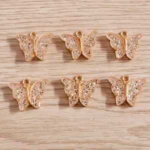 Detail of six gold-plated butterfly charms with glitter inlay on wooden background