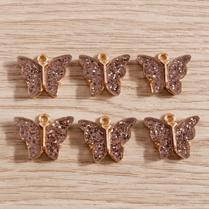 Detailed macro view of 6 gold alloy butterfly pendants with sparkling glitter resin inlay