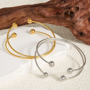 Minimalist 18k gold and silver cuff bracelets with polished spheres on stone and wood base