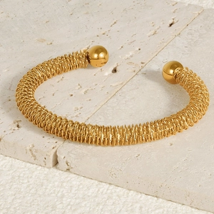 Detailed macro view of 18k gold coil bracelet with intricate woven texture and metal spheres