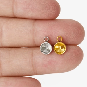 Makroaufnahme von kleinen Gold- und Silber-Anhängerbasen für DIY-Schmuck auf einem Finger