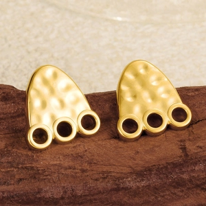 Close-up of golden paw print stud earrings with hammered metal texture on wooden surface