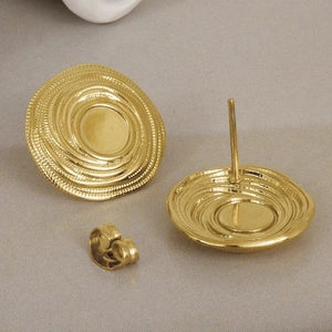 Dettaglio di orecchini a spirale in oro 18k con texture in acciaio inossidabile e chiusure a farfalla