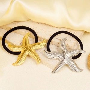 Detail view of gold and silver starfish charms on black elastic hair ties on silk background