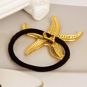 Close-up of 18k gold-plated starfish detail on black elastic hair tie with marble background