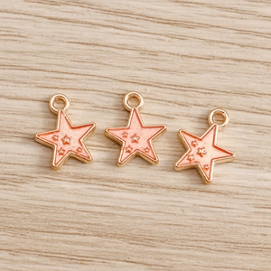 Macro detail of three pink enamel star pendants with golden alloy frames on wood