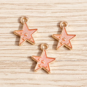 Macro shot of three star-shaped alloy pendants with pink enamel oil and gold star accents