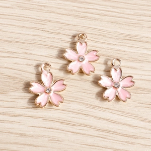 Macro shot of three pink enamel cherry blossom charms with center crystals on wood