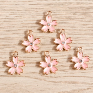 Close-up of pink enamel cherry blossom charms with gold edges and center crystal detail