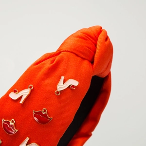 Détail d'un serre-tête noué orange avec des breloques émaillées de lèvres et talons hauts