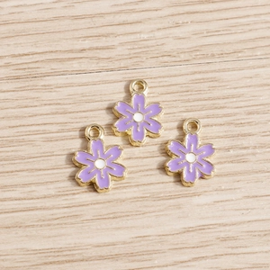 Détail de trois breloques fleurs violettes avec bord doré sur une surface en bois clair