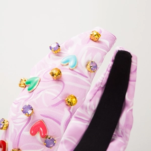 Dettaglio del cerchietto in tessuto rosa-viola con strass e ciondoli a forma di cuore