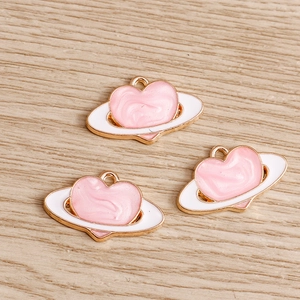 Dettaglio dei ciondoli a pianeta cuore in smalto rosa con base in metallo dorato per fai-da-te