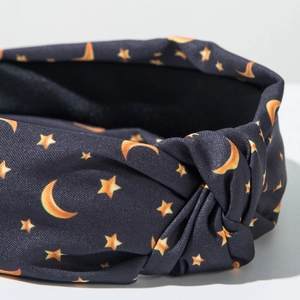 Detail of a dark fabric knotted headband featuring bright orange star and moon prints