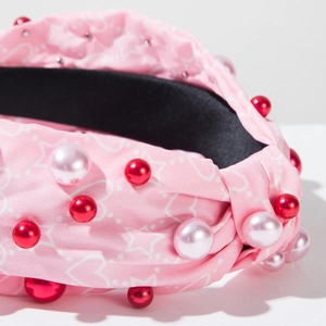 Détail d'un serre-tête en tissu rose avec motifs étoiles, nœud et perles élégantes
