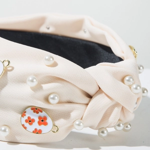 Detail eines rosa Stoffstirnbands mit weißen Perlen und einem Emaille-Blumenanhänger